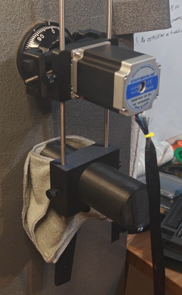 LockManipulator Auto Dialer: NEMA 23 stepper motor on two steel rods over a safe dial, held by a magnetic leg resting on a towel