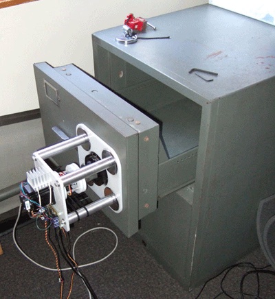 The first Vogt and Jordan robot: a stepper motor and servo head on aluminium columns mounted on the drawer of an opened grey filing safe